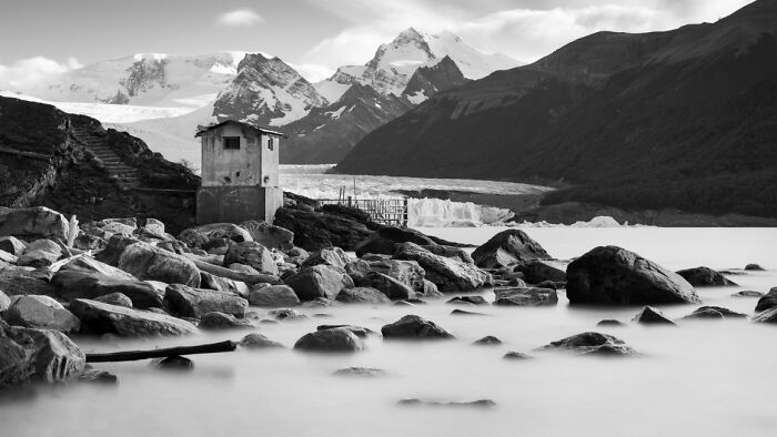 Black and white landscape with mountains, rocks, a small building, and calm water in stunning animal photos from Exposure One awards.