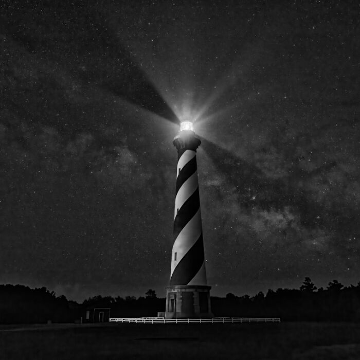 Black and white photo of a lighthouse shining brightly under a star-filled night sky for stunning animal photos SEO.