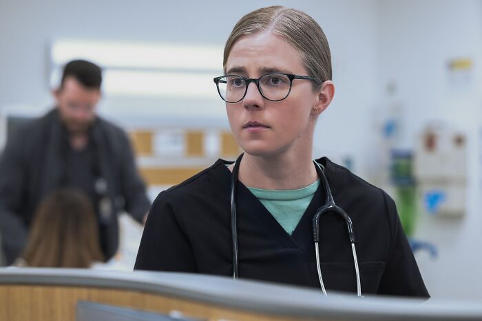 Female medical professional wearing glasses and stethoscope, focusing intently in a hospital setting, depicting medical drama disorder.