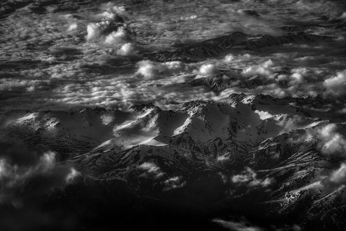 A breathtaking aerial view of snow-covered mountain peaks partially shrouded by clouds during twilight.