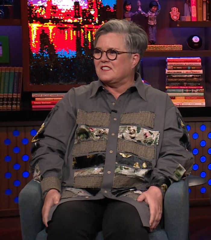 Person with short gray hair and glasses sitting in a studio, discussing experiences with diva movie set workers.