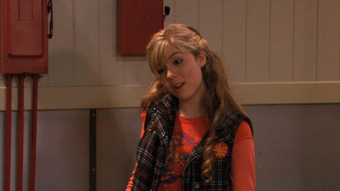 Young female celebrity indoors wearing a plaid vest and red shirt, representing celebrities who didn’t deserve their downfall.