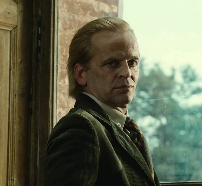 Middle-aged male actor in vintage attire looking serious near window, representing movie set workers dealing with diva stars.