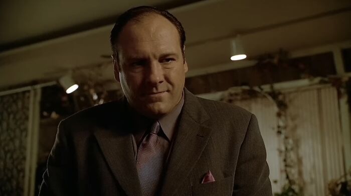Man in a dark suit and tie smirking in a dimly lit room, representing famous villains and pure evil themes.
