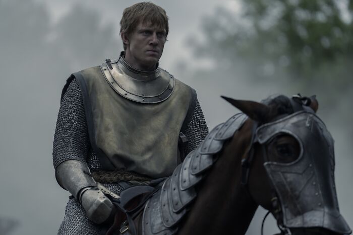 A hedge knight in armor rides a horse through a misty forest, representing a wandering knight in the Seven Kingdoms.