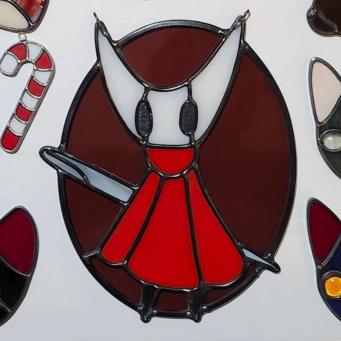 Stained glass sign depicting a pop culture icon wearing a red dress with white ears on a dark circular background.