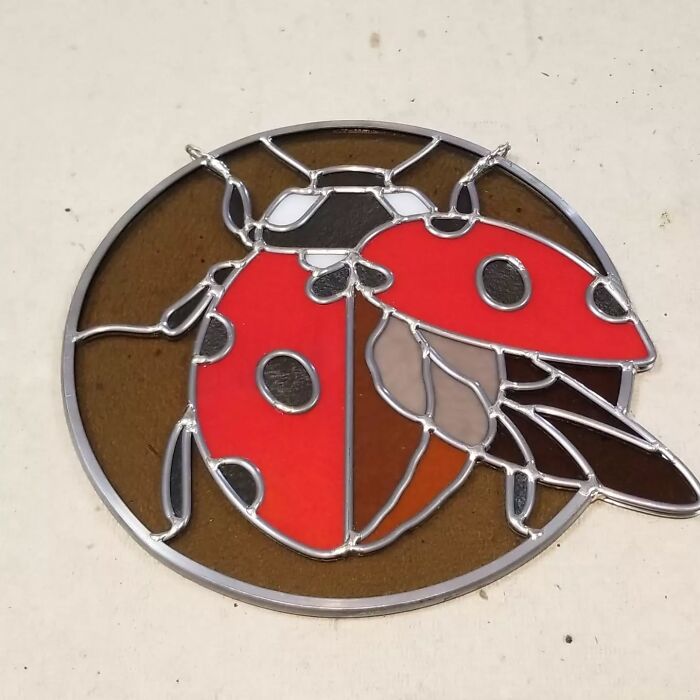Vivid stained glass sign of a red ladybug with black spots on a brown background, showcasing pop culture icon style.