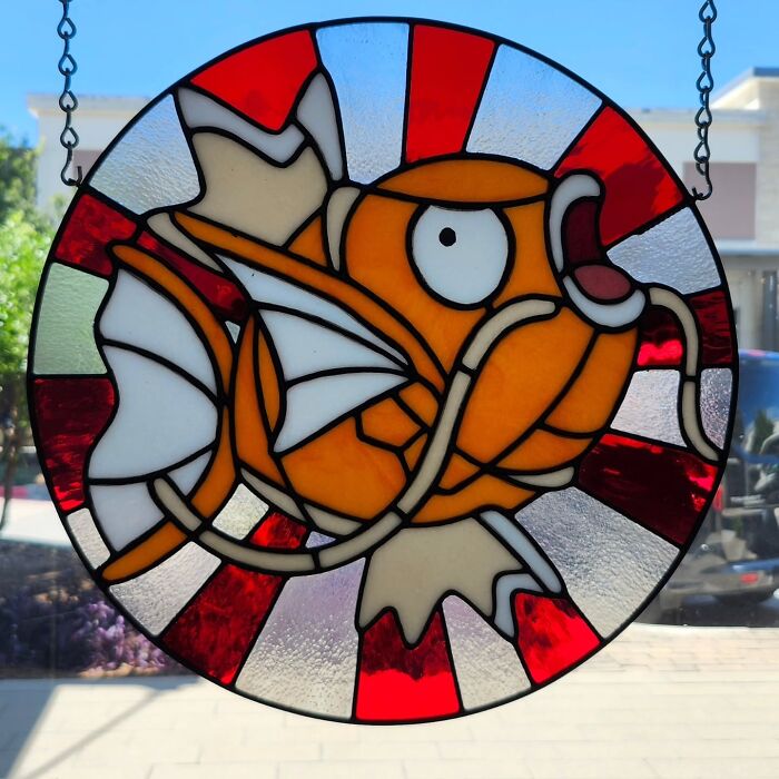 Stained glass sign of a vivid orange pop culture fish icon with red and white background hanging by chains.