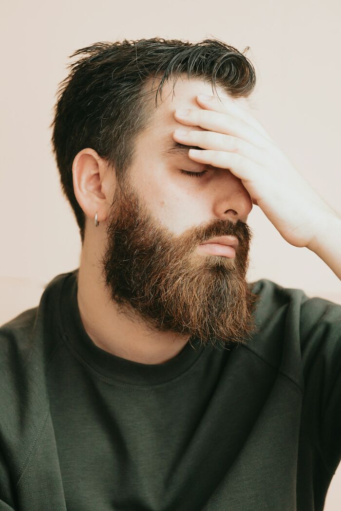 Man with beard and earring covering face expressing panic after accidental texts causing stress and worry.