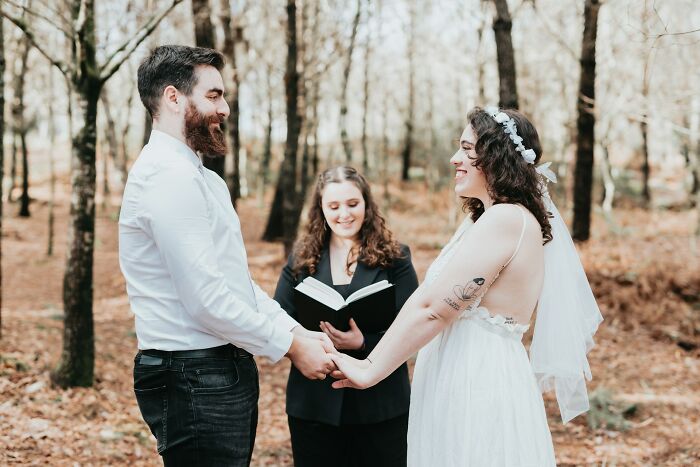 Couple holding hands during an outdoor wedding ceremony with an officiant in a woodland setting, capturing wedding moments.
