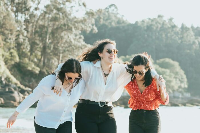 Three women walking outdoors by the water, smiling and enjoying normal American behaviors that might be offensive elsewhere.