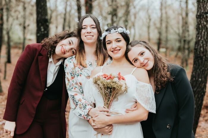 Bride holding bouquet with bridesmaids smiling outdoors in forest setting capturing wedding moments.