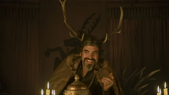 Man wearing antler crown and fur cloak in dimly lit room, representing a house sigil in Knight of the Seven Kingdoms. Man wearing antler crown and fur cloak in dimly lit room, representing a house sigil in Knight of the Seven Kingdoms.
