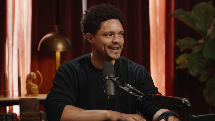 Comedian speaking into a microphone in a studio setting, highlighting celebs who weren’t nepo babies and rose on their own.