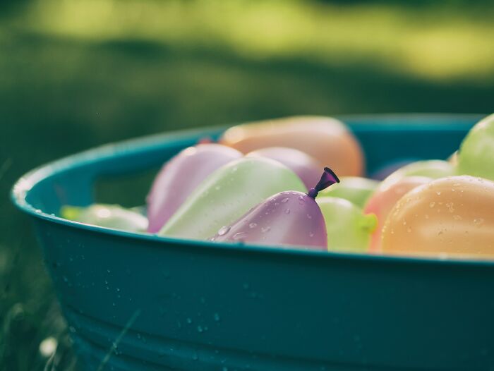 Colorful water balloons in a blue tub outdoors, representing high school summer fun and related controversies.