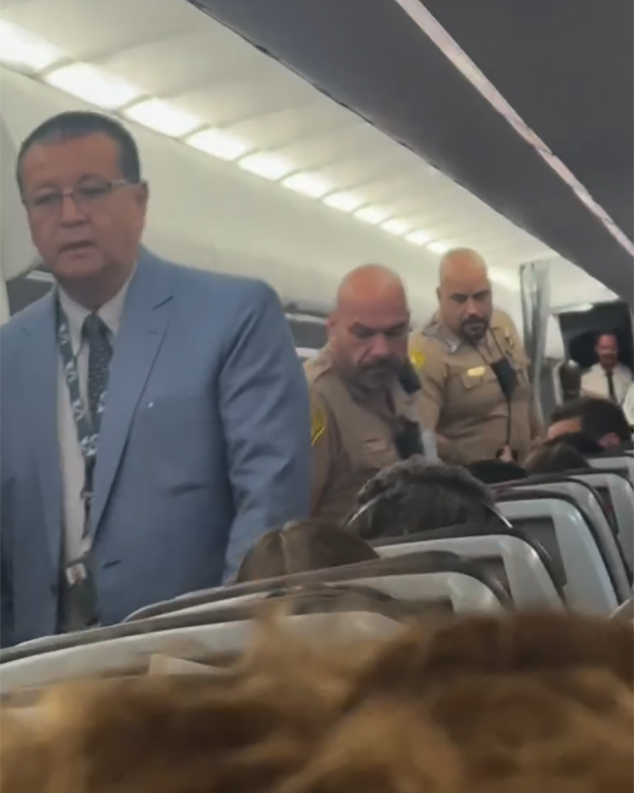Flight attendants and officers escorting adult stars during first-class seat refusal incident on airplane cabin interior. Flight attendants and officers escorting adult stars during first-class seat refusal incident on airplane cabin interior.