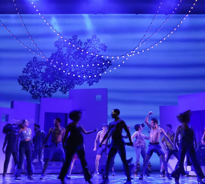 Male Karen in Mamma Mia Broadway scene, man angrily confronting audience amid blue-lit dancers and string lights