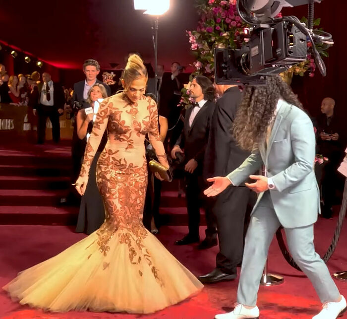 Jennifer Lopez in an elaborate gown at Golden Globes with a man gesturing, a moment sparking backlash over rude interaction. Jennifer Lopez in an elaborate gown at Golden Globes with a man gesturing, a moment sparking backlash over rude interaction.