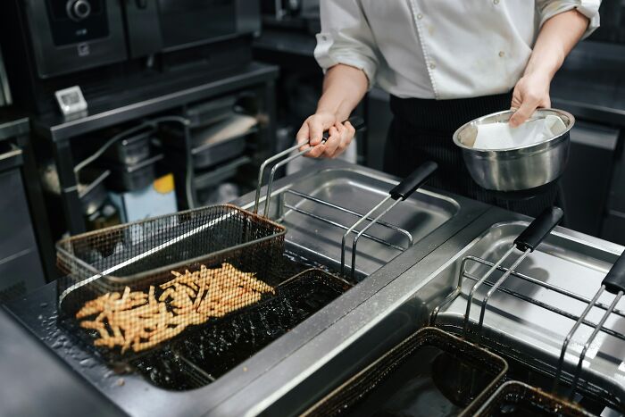 Person frying French fries in a commercial kitchen, illustrating coworker stories of unhinged behavior at work.