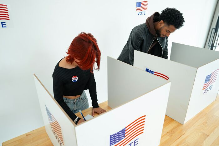 Two people voting in booths, focused on ballots, illustrating accidental texts that sent these people into a panic.