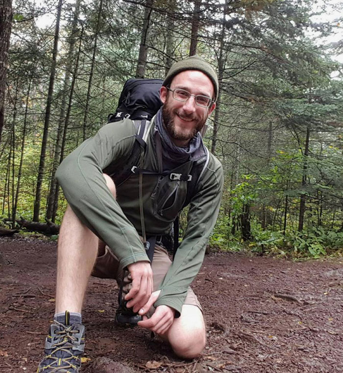 Man wearing glasses and hiking gear kneeling on a forest trail reflecting the story about Alex Pretti’s fate and government care. Man wearing glasses and hiking gear kneeling on a forest trail reflecting the story about Alex Pretti’s fate and government care.