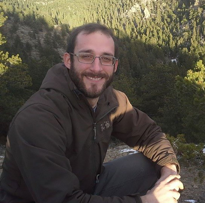 Man wearing glasses and a brown jacket sitting outdoors in front of a forest, relating to Alex Pretti government care story. Man wearing glasses and a brown jacket sitting outdoors in front of a forest, relating to Alex Pretti government care story.
