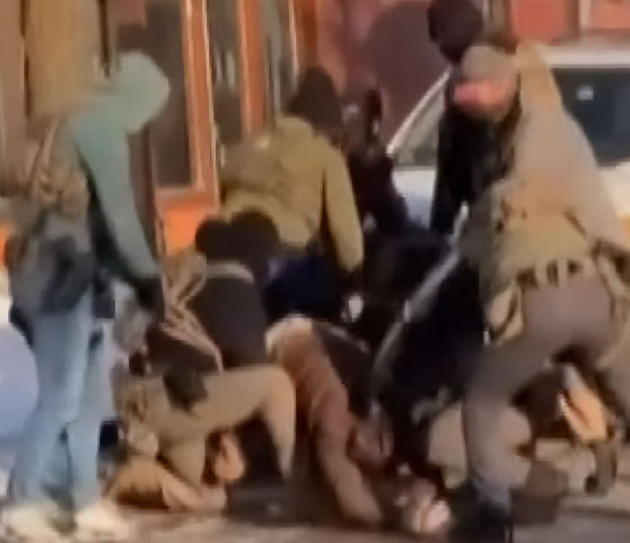 Police officers detain a person on the ground during a chaotic street altercation, highlighting tensions in government response.