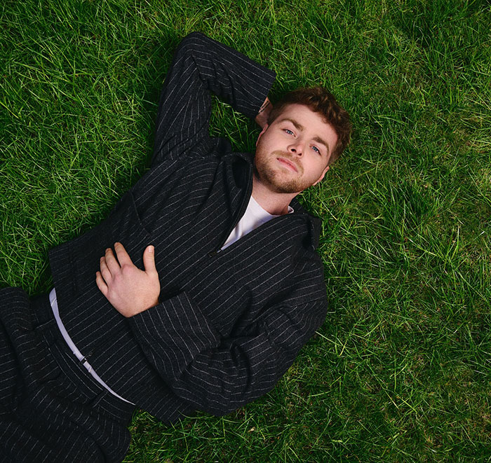 Young man in a pinstripe suit lying on grass, reflecting on Grammy snubs and their impact on fans and artists.
