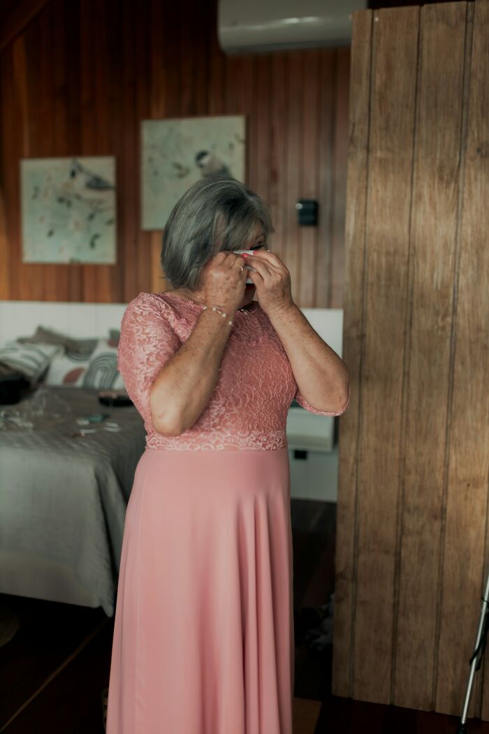 Older woman in a pink dress wiping tears in a cozy room, reflecting emotions tied to a surprising DNA test plot twist.