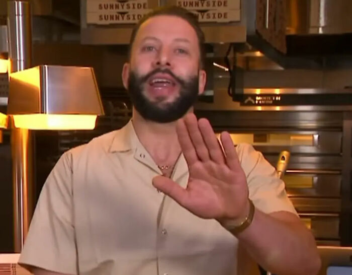 Pizzeria owner with beard and beige shirt in restaurant kitchen known for his salty replies to harsh online reviews. Pizzeria owner with beard and beige shirt in restaurant kitchen known for his salty replies to harsh online reviews.