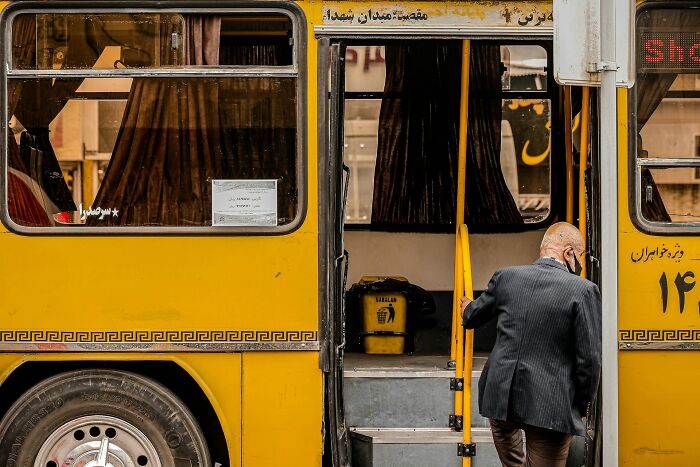 An elderly man entering a yellow bus with open doors, illustrating patient and doctor unethical behavior concepts.