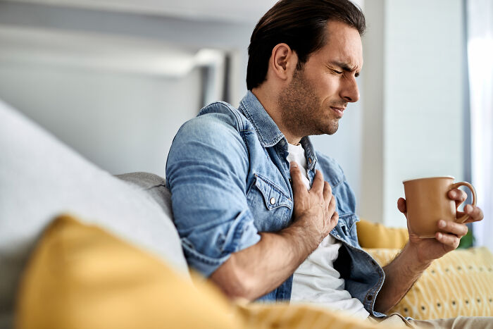 Man sitting on couch holding mug and clutching chest in discomfort, illustrating all you can eat buffet gluttony effects.