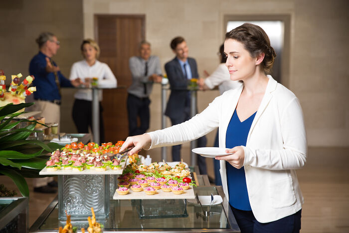 Woman serving herself at an all you can eat buffet with various appetizers as employees watch in the background.