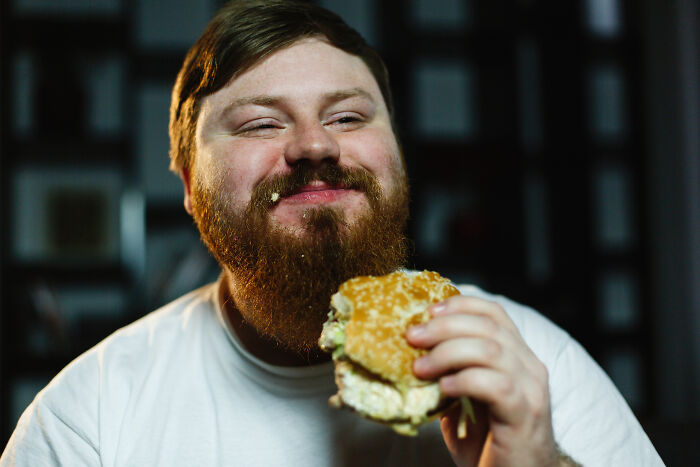 Man with a beard eating a large burger at an all you can eat buffet showing gluttony and indulgence.