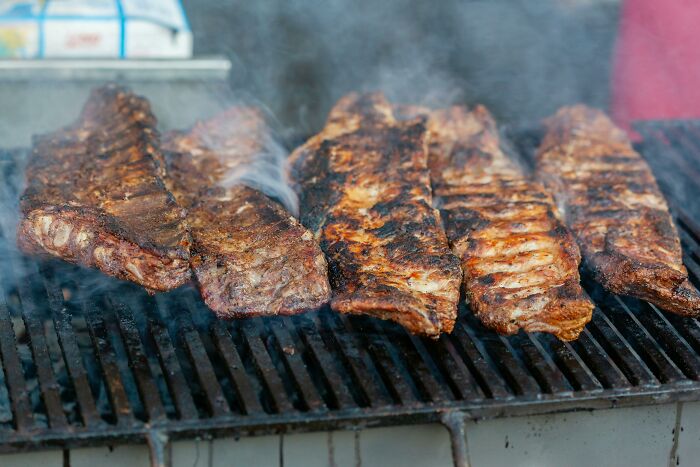 Grilled ribs cooking on a barbecue grill with smoke rising, illustrating all you can eat buffet gluttony.