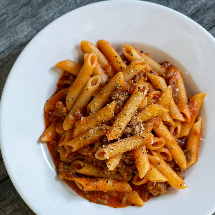 Plate of penne pasta with tomato sauce and ground meat, illustrating all you can eat buffet gluttony experiences.
