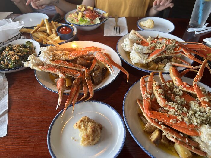 Seafood feast at an all you can eat buffet with crab legs, fries, salad, and various side dishes on a wooden table.