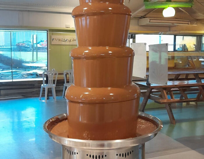 Chocolate fountain at an all you can eat buffet with empty chairs and tables in the background