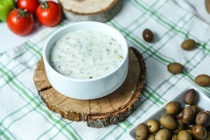 Bowl of creamy dip on wooden coaster surrounded by olives and tomatoes, related to all you can eat buffet gluttony.