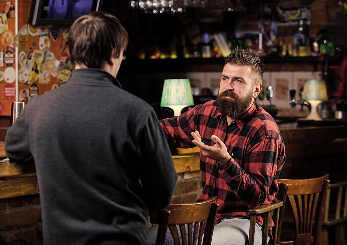 Two men talking in a dimly lit bar, illustrating all you can eat buffet employees sharing gluttony experiences.