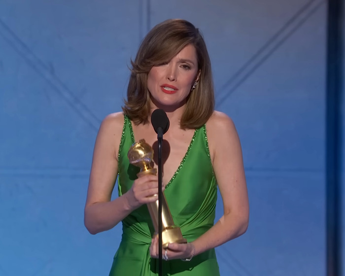 Amanda Seyfried in a green dress holding a Golden Globe award, reacting during her speech at the awards ceremony.