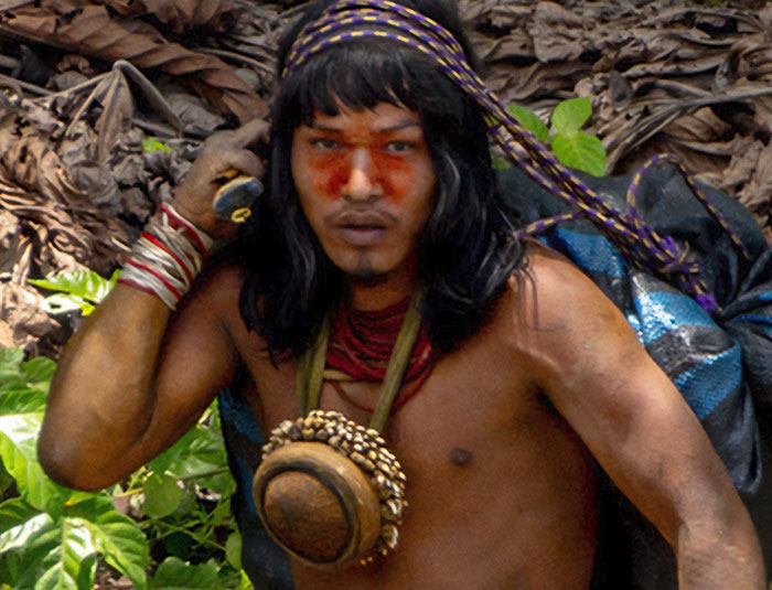 Uncontacted Amazonian tribe member with traditional face paint and accessories in the dense jungle environment.
