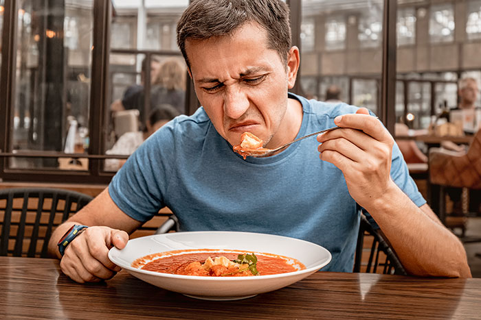 Man making faces reacting to traditional gross food served instead of American dishes in restaurant setting