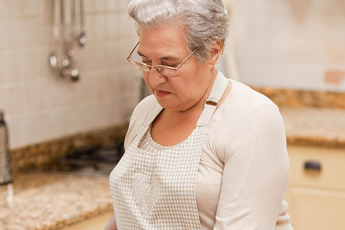 Older woman in apron making faces reacting to traditional gross food in a kitchen setting Older woman in apron making faces reacting to traditional gross food in a kitchen setting