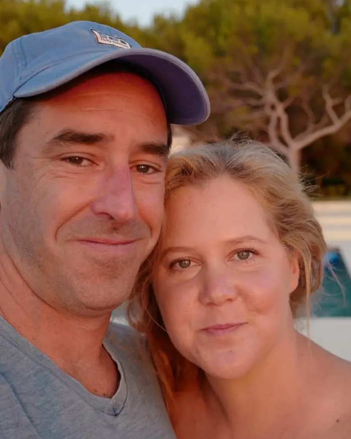 Amy Schumer and a man posing together outdoors, reflecting on her trolling herself after divorce filing. Amy Schumer and a man posing together outdoors, reflecting on her trolling herself after divorce filing.