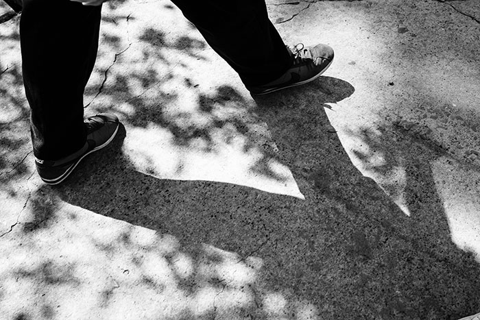 Man's feet walking on pavement casting shadow, representing guy learns girlfriend is landlord and demands profits. Man's feet walking on pavement casting shadow, representing guy learns girlfriend is landlord and demands profits.