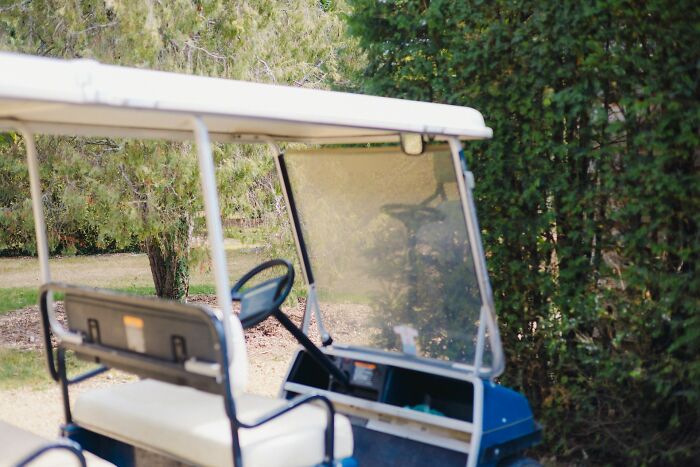 Empty golf cart parked near trees in public showing a weird and shocking scene with zero shame displayed.