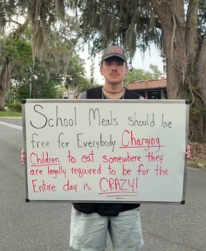 Young man holding a sign calling out world issues, advocating for free school meals for all children.