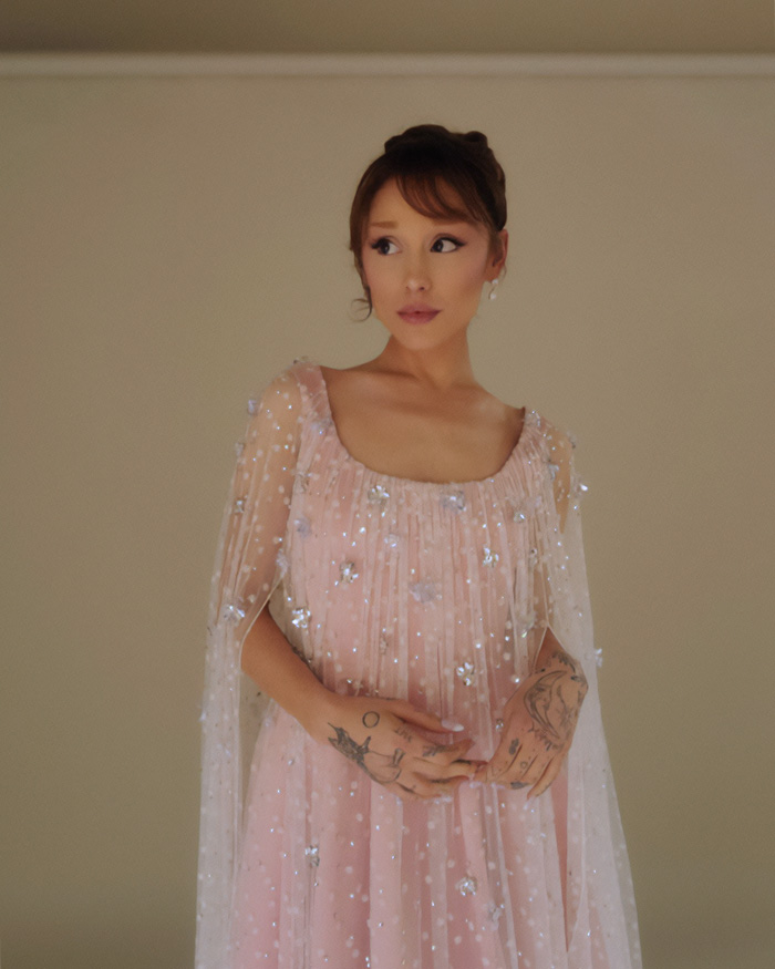 Ariana Grande in a sparkly pink dress with tattoos visible on her hands, showcasing a stunning transformation look. Ariana Grande in a sparkly pink dress with tattoos visible on her hands, showcasing a stunning transformation look.