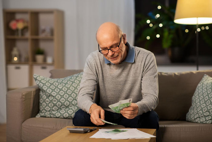 Elderly man counting cash at home with calculator and bills, concerned about parents house payment Elderly man counting cash at home with calculator and bills, concerned about parents house payment